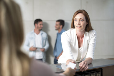 Businesswoman speaking to receptionist over counter - ZEF003134