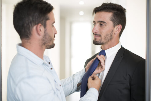Lässig gekleideter Mann, der die Krawatte seines Zwillingsbruders im Büro zurechtrückt - ZEF003140