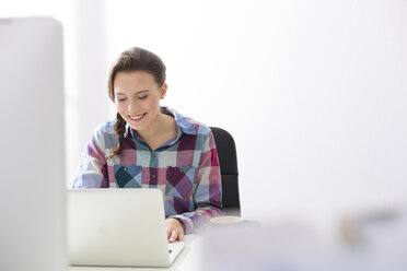 Lächelnde junge Frau mit Laptop am Schreibtisch - WESTF020495