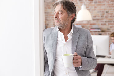 Businessman holding cup of coffee in office - WESTF020523