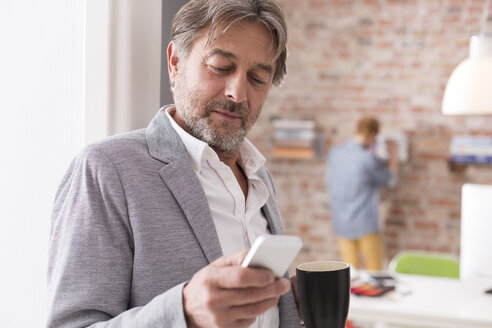 Geschäftsmann mit Mobiltelefon und einer Tasse Kaffee im Büro - WESTF020525