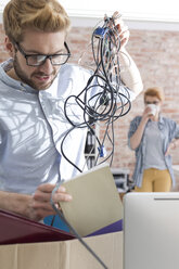 Junger Mann mit Kabelgewirr im Büro - WESTF020548