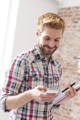 Smiling young man with cell phone in office - WESTF020672