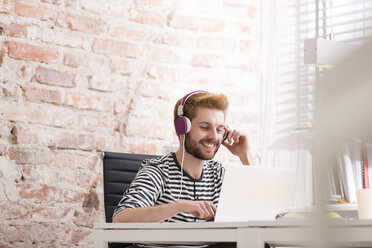 Smiling young man with headphones at desk - WESTF020598