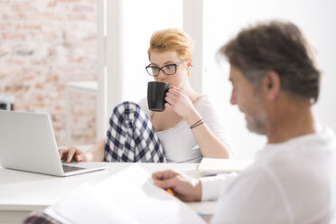 Young woman in pajamas using laptop with man reading - WESTF020622