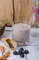 Glass of blueberry smoothie, fresh curcuma, wooden shovel of chia seeds and blueberries on wood - ODF001015