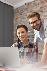 Smiling young woman and man with laptop in office - WESTF020607