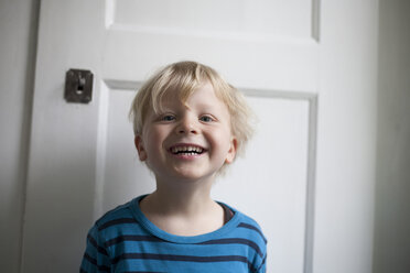 Porträt eines lachenden kleinen Jungen vor einer weißen Tür - RB002236