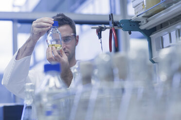 Wissenschaftlerin im mikrobiologischen Labor betrachtet Flüssigkeit in einer Flasche - SGF001298