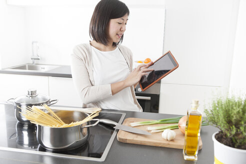 Lächelnde junge Frau, die beim Kochen ein digitales Tablet benutzt - FLF000798