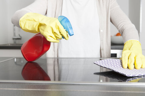Woman wearing gloves cleaning ceramic glass cooktop with spray - FLF000807