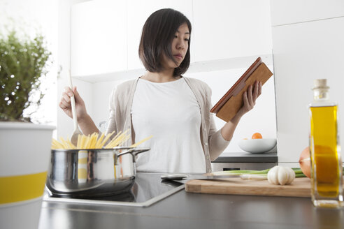 Junge Frau benutzt digitales Tablet beim Kochen von Spaghetti - FLF000809