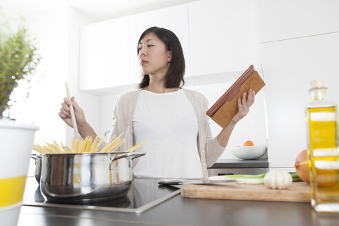 Junge Frau hält digitales Tablet beim Kochen von Spaghetti - FLF000810