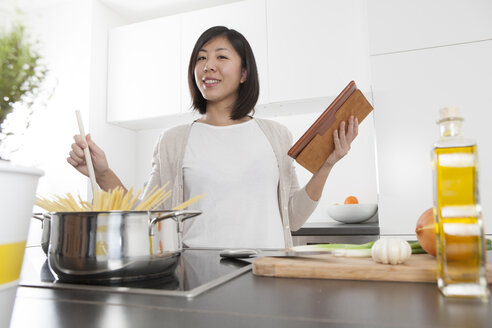Lächelnde junge Frau hält ein digitales Tablet, während sie Spaghetti kocht - FLF000815