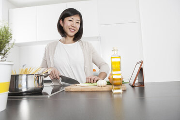 Porträt einer lächelnden jungen Frau beim Schneiden von Frühlingszwiebeln in der Küche - FLF000811