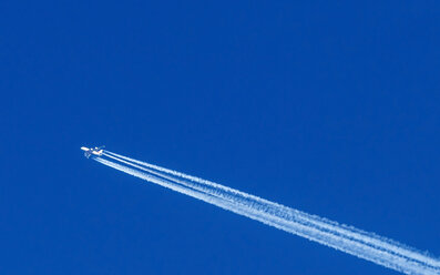 Fliegendes Flugzeug und Dunstschleppe vor blauem Himmel - EJWF000637