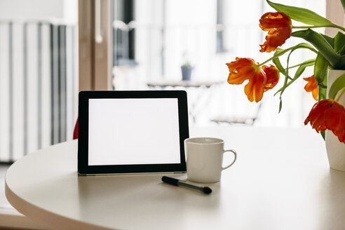 Tablet PC, Stift und eine Kaffeetasse auf einem weißen runden Tisch mit roten Tulpen - MFF001393