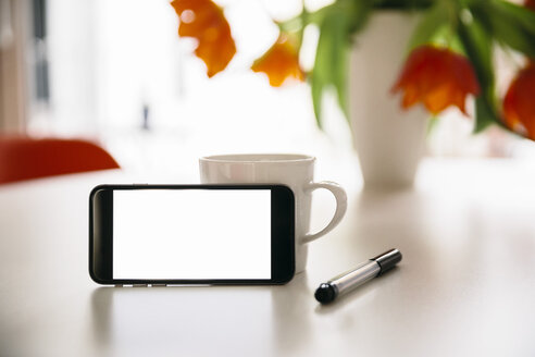Smart Phone lehnt an einer Kaffeetasse auf einem weißen runden Tisch mit roten Tulpen - MFF001394