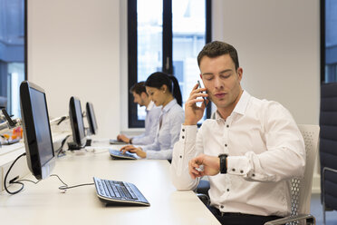 Man at desk on cell phone with colleagues in background - SHKF000198