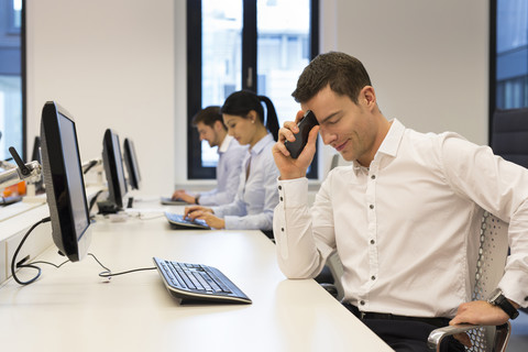 Frustrierter Mann am Schreibtisch mit Kollegen im Hintergrund, lizenzfreies Stockfoto