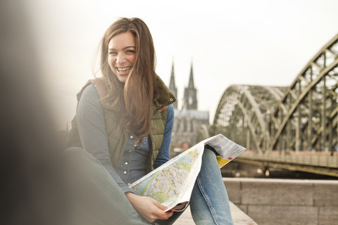 Deutschland, Köln, Porträt einer lächelnden jungen Frau mit Stadtplan auf dem Knie, lizenzfreies Stockfoto
