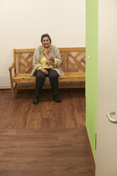 Demenzkranke ältere Frau auf einer Bank in einem Pflegeheim sitzend - DHL000516