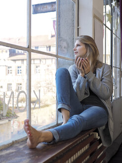 Junge Frau mit Teeschale auf dem Fensterbrett sitzend - LAF001280