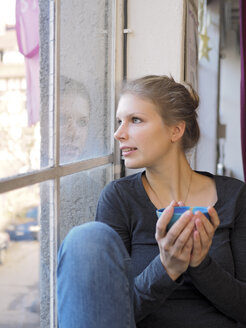 Junge Frau mit Teeschleife schaut durch ein Fenster - LAF001281