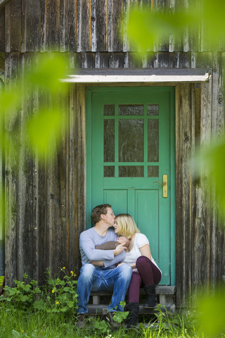 Glückliches Paar mit Neugeborenem vor dem Haus sitzend, lizenzfreies Stockfoto