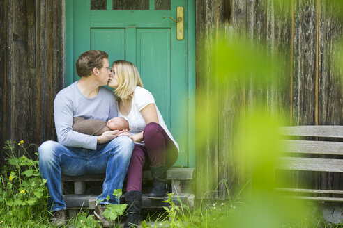 Küssendes Paar mit Neugeborenem vor einem Haus sitzend - JTLF000036