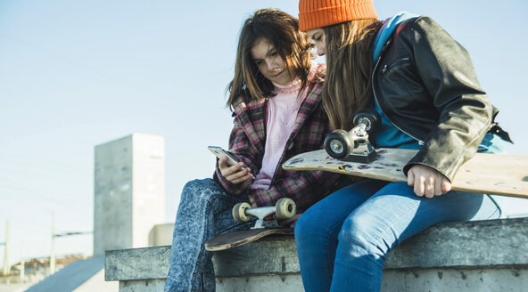 Two girls in skatepark sharing cell phone - UUF003035