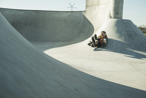 Teenage girl with cell phone and headphones in skatepark - UUF003051
