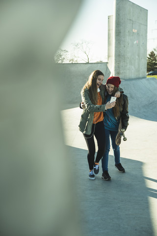 Zwei glückliche Teenager-Mädchen mit Handy im Skatepark, lizenzfreies Stockfoto