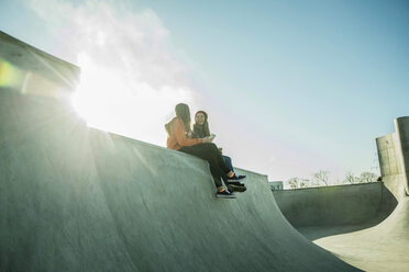 Zwei Teenager-Mädchen im Skatepark teilen sich ein Mobiltelefon - UUF003083