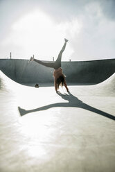 Teenage girl doing a cartwheel in skatepark - UUF003084