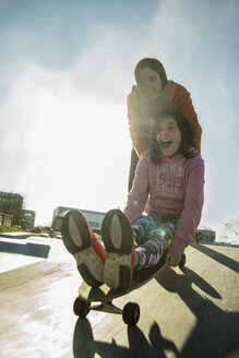 Teenage girl pushing girl on skateboard - UUF003086