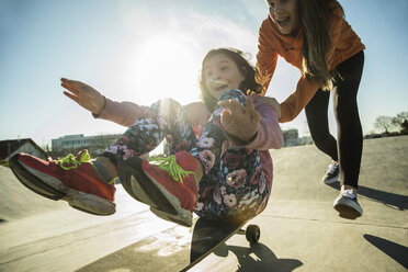 Teenage girl pushing girl on skateboard - UUF003068