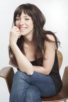 Portrait of smiling woman with dark long hair sitting on a chair - PATF000008