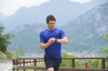 Italy, Trentino, man running on road near Lake Garda checking the time - MRF001460