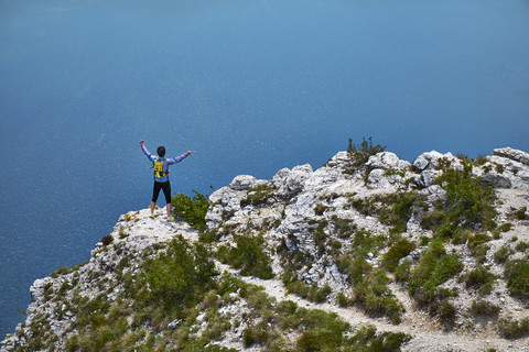Italien, Trentino, Mann jubelt auf Berg am Gardasee, lizenzfreies Stockfoto