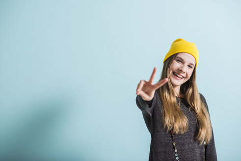 Laughing female teenager showing victory-sign wearing yellow cap - UUF003106