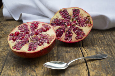 Two halves of a pomegranate and tea spoon on wood - LV002622