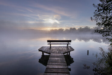 Germany, Bavaria, Wessling, Wesslinger See, boardwalk with wooden bench in the morning mist - MBOF000028