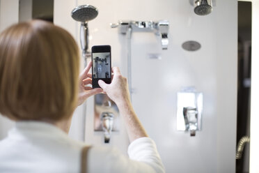 Frau fotografiert mit ihrem Smartphone die Wasserhähne in einem Sanitärgeschäft - ZEF003978