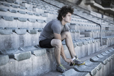 Young sportsman sitting on grandstand of a stadium tying his shoes - ZEF004590