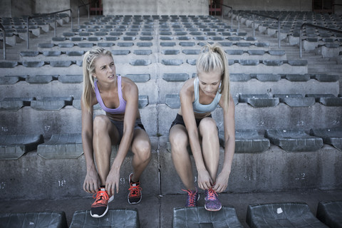 Zwei Sportlerinnen sitzen auf der Tribüne eines Stadions und binden ihre Schuhe, lizenzfreies Stockfoto
