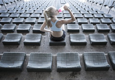 Sportlerin sitzt auf der Tribüne eines Stadions und trinkt Wasser, lizenzfreies Stockfoto
