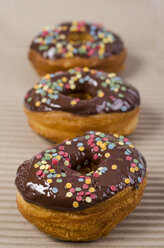 Row of three American cronuts with chocolate icing and sugar confetti - OD001064