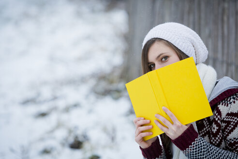 Junge Frau versteckt sich hinter gelbem Buch - JTLF000041