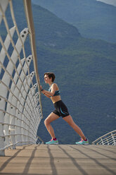 Italy, Trentino, woman stretching on bridge at Lake Garda - MRF001524